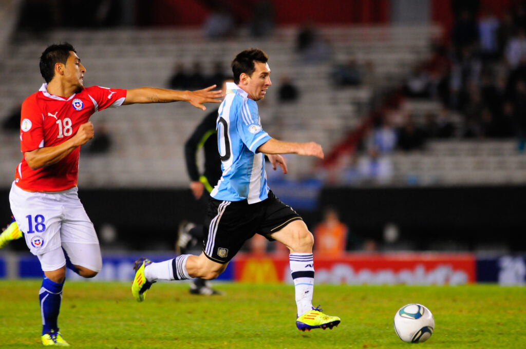 Un jugador Chileno intenta alcanzar a Messi que corre con el balón en sus pies.