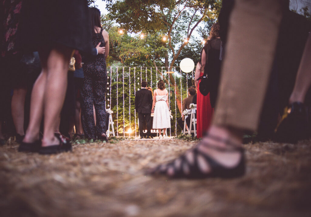 Una pareja, en segundo plano, durante la ceremonia de su casamiento. En el primer plano se observa varios pies de los invitados.