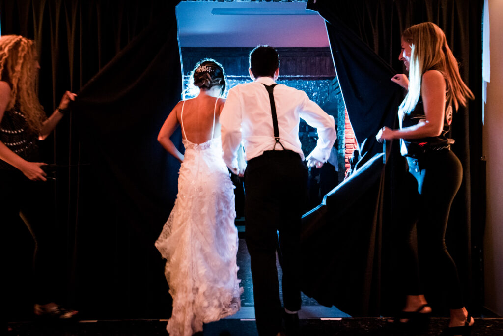 Una pareja, de espaldas, entra corriendo a la fiesta de su casamiento cuando se abre el telón.