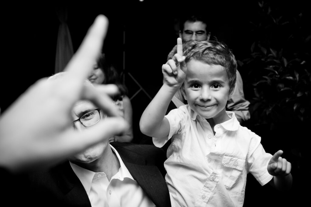 Un niño, a upa del padre, baila en segundo plano señalando para arriba, al igual que la mano que aparece en primer plano.