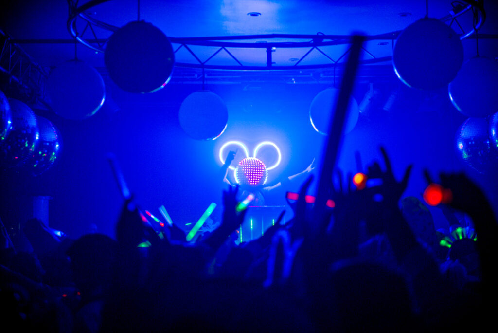 Fiesta de 15 años, donde mucha gente baila, y en el centro de la imagen aparece un DJ con una máscara de Mickey iluminada con luces led.
