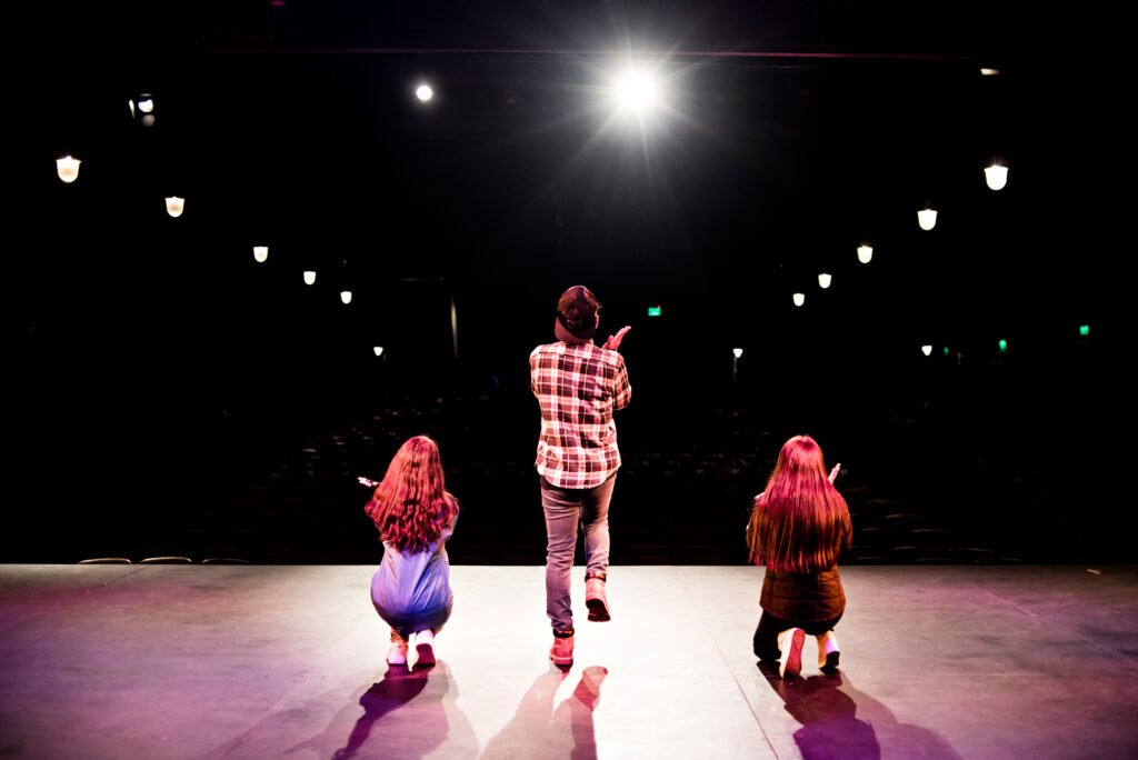 3 participantes bailan y cantan en el escenario. El varón está de pie en el centro y las dos mujeres agachadas, una de cada lado, durante la coreografía.