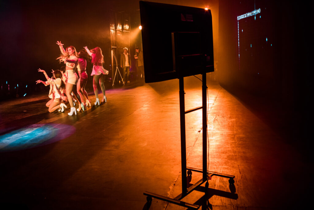 En el margen superior izquierdo, un grupo de bailarinas realiza su show en el escenario