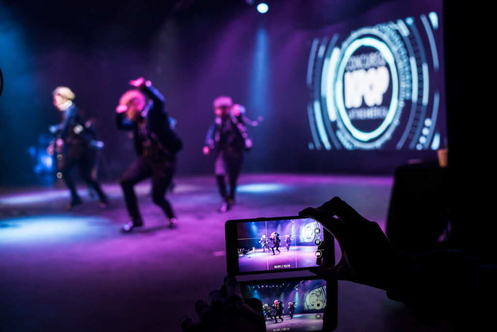 Una persona graba con dos celulares en primer plano al grupo ganador del concurso de K-Pop en Argentina.