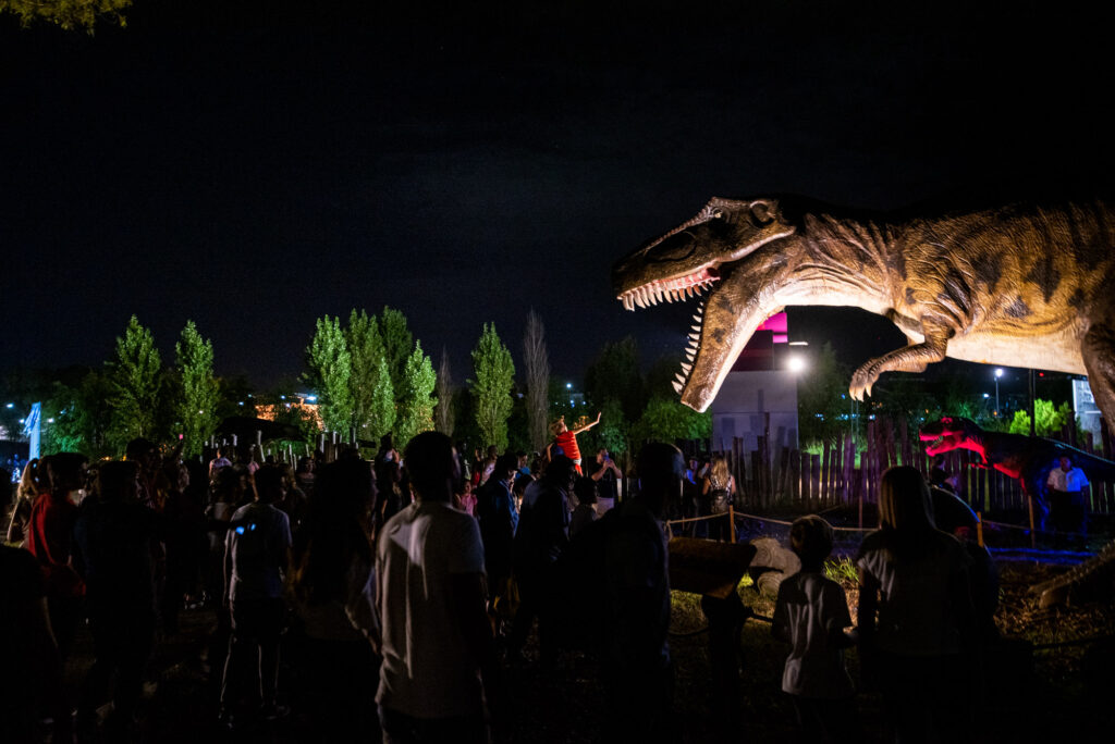 Un grupo numeroso de personas observa un dinosaurio animatrónico en la megamuestra Tecnópolis.