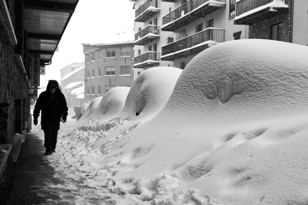 Una persona camina por la calle al lado de cuatro autos todos cubiertos de nieve.