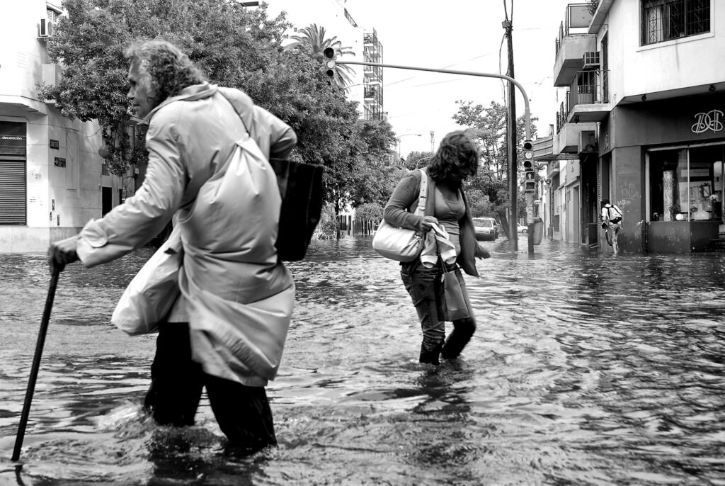 3 personas caminan por una calle inundada con el agua hasta las rodillas.