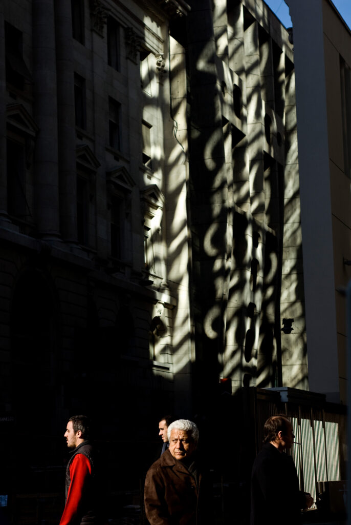 4 personas caminan por el Microcentro Porteño entre luces y sombras de los edificios.